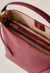 Borsa a mano in pelle borgogna con texture liscia, hardware dorato, tasca con zip e fodera beige. Include una tracolla rimovibile.