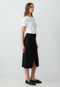 Witte korte mouw top gecombineerd met een zwarte midi rok met een split aan de voorkant, aangevuld met zwarte instappers met decoratieve hardware accenten.