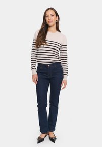 Randig tröja i beige och svart, matchad med mörkblå jeans. Har en åtsittande design och spetsiga svarta skor med rosettdetaljer.
