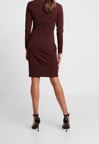 Tajta vinröd klänning med långa ärmar, knä-lång fåll och slät textur. Bärs med svarta lackskor med hög klack.