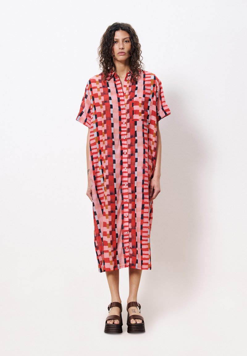 Kurzärmliges, knöpfbares Kleid mit einem lebendigen geometrischen Muster in Rot und Pink. Hergestellt aus leichtem Stoff, mit einem lässigen Schnitt und knielanger Länge.