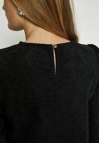 Black corduroy top featuring a textured ribbed design, rounded neckline, and a back closure with a metallic button.