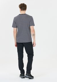 Námořnické a bílé pruhované tričko s krátkým rukávem, zkombinované s černými kalhotami a tmavou obuví, odhalující tetování na levém paži.