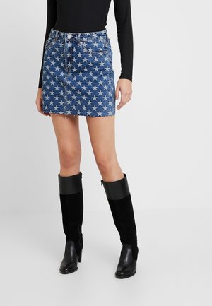Denimowa mini spódniczka w gwiazdkowy wzór w odcieniach niebieskiego, z postrzępionym wykończeniem i przednimi kieszeniami. Połączona z czarnymi kozakami za kolano.