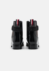 Bottines en cuir verni noir au design épuré, dotées d'un talon robuste et d'une sangle ajustable avec le logo "TOM TAILOR". Accent rouge et blanc sur les sangles.