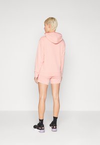 Lys rosa hettegenser og matchende shorts, med myk stoff, hette og teksturerte detaljer, kombinert med svarte og rosa joggesko.