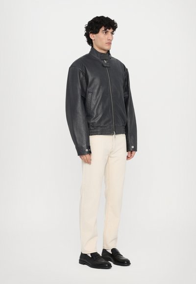 Veste bomber noire en cuir avec col montant, fermeture éclair à l'avant et poches latérales. Comprend une taille et des poignets élastiques pour un look ajusté.