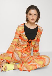 Top cropped de mangas longas e calças combinando em padrões vibrantes de laranja, amarelo e rosa; apresenta um top interior preto e detalhes com cordão.