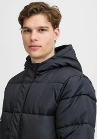 Chaqueta de plumas negra con capucha, patrón acolchado y textura lisa y brillante. Cierre con cremallera y puños elásticos para un ajuste ceñido.