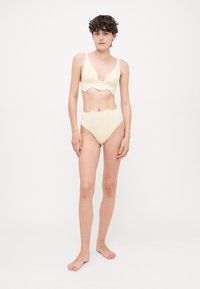 Helle gelbe Zweiteiler-Badeanzug mit einem gewellten Design oben und einer hochgeschnittenen Unterhose. Hergestellt aus einem dehnbaren Stoff.