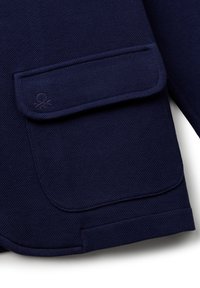 Granatowa kurtka o teksturowanej powierzchni z dużą kieszenią na klapie, strukturalnym fasonem i subtelnym logo na kieszeni, wykonana z trwałego materiału.