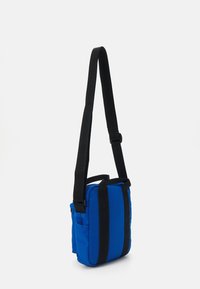 Bolsa transversal azul com alças pretas, formato retangular, tecido texturizado, bolso frontal e alça ajustável. Design compacto para fácil transporte.
