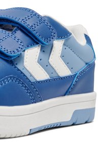 Blaue synthetische Sneakers mit weißen und hellblauen Chevron-Akzenten, Klettverschlussriemen und einer strukturierten Gummisohle mit blauem Profil.