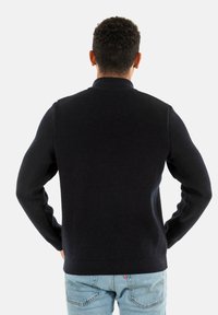 Maglione a coste blu navy con colletto alzato e maniche lunghe, abbinato a jeans di denim azzurro. Il maglione presenta un tessuto testurizzato.