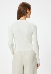 Prążkowany longsleeve w kolorze ecru, z okrągłym dekoltem i dopasowanymi mankietami. Miękka faktura z wąskim krojem, w zestawieniu z jasnymi spodniami.
