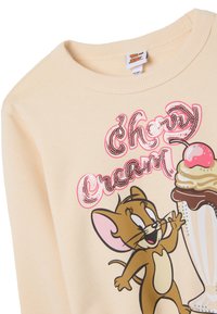 Sudadera beige con un ratón de dibujos animados, texto "Cherry Cream" en brillantes lentejuelas y un gráfico de batido con una cereza en la cima.