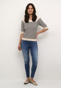Maglione a righe in beige e blu navy, con maniche corte e scollo tondo, abbinato a jeans skinny azzurri e ballerine beige.