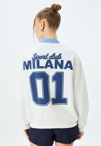 Sudadera blanca con texto azul que dice "Club Deportivo MILANA 01" en la parte posterior. Presenta un cuello redondo y puños de canalé, fabricada con tejido suave.