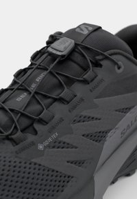 Zwarte sportschoen met een combinatie van gaas en synthetische materialen, een gestructureerd oppervlak, een gesloten vetersysteem en een opvallend "GORE-TEX"-logo.