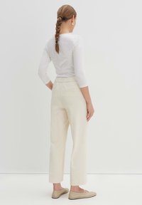 Weißes, eng anliegendes Langarmoberteil, kombiniert mit cremefarbenen Cordhosen mit geradem Schnitt und Seitentaschen. Schlichte beige Ballerinas.