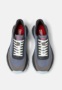 Zapatillas deportivas con una parte superior textil en tonos gris y azul, acentos negros, cordones blancos y una suela de goma texturada en un azul claro. Logo rojo en la lengüeta.