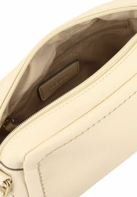 Interior de un bolso de cuero color crema que presenta un compartimento con cremallera y un forro suave, con una pequeña etiqueta de marca visible.