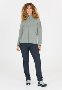 Fleece-takki vaaleanharmaana, jossa vetoketju ja vaaleanpunaiset yksityiskohdat, yhdistetty tummansinisiin housuihin ja harmaisiin vaelluskengiin, esittelee käytännöllisen ulkoiluilmeen.