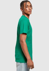 Camiseta de algodón verde con cuello redondo y mangas cortas, con un corte recto y detalles de costuras visibles.