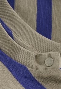 Beige en blauw gestreepte gebreide stof met een ronde halslijn, voorzien van een kleine grijze knop met een reliëf van een klavertje vier.