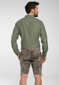 Grünes Hemd mit Knopfleiste aus strukturiertem Stoff, kombiniert mit braunen Leder-Shorts mit seitlichen Schnürungen und einem Taillenbund.