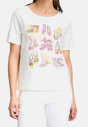 Kvinde iført hvid t-shirt med farverige illustrerede sko, herunder sneakers, høje hæle og sandaler i pink, gule og orange toner.