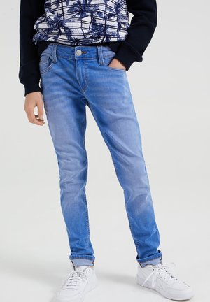 Blå denimjeans med slank pasform, med let falmning og slidte detaljer. Kombineret med hvide sneakers og en mønstret sweatshirt.