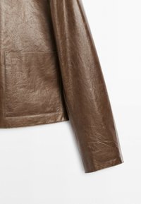 Manche de veste en cuir marron avec texture visible et poche à rabat rectangulaire sur le côté inférieur, sur fond blanc.