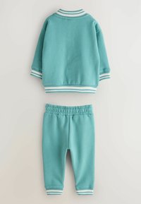 Tyrkysová tepláková súprava s krátkym rukávom na bundu a nohavicami s elastickým pásom. Obsahuje biele pruhy na manžetách a golieri. Mäkká tkanina.