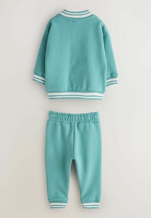 Türkiissinine dressipluus lühikeste varrukate ja elastse vöökohaga pükstega. Mansettidel ja krae ääres valged triibud. Pehme kangas.