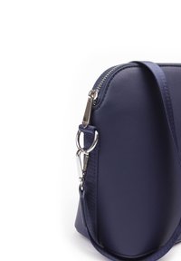 Marineblaue Leder-Crossbody-Tasche mit silbernen Beschlägen, Reißverschluss und verstellbarem Stoffgurt. Geschwungene Form und glatte Textur.