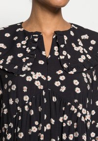 Vestido preto floral com margaridas brancas e detalhes em laranja. Apresenta um colarinho com babados, fecho de zipper e cintura franzida para um ajuste solto.