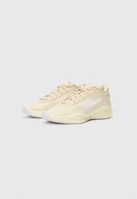 Beige atletiksko med en struktureret mesh-overdel, tonale snørebånd og et hvidt swoosh-logo. Afrundet tå, polstret sål med subtilt grebmønster.