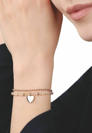 Muñeca con dos delicadas pulseras de cuentas, una con un pequeño colgante en forma de corazón, sobre un fondo de camiseta negra de manga larga.