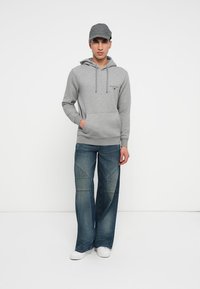 Gray hoodie with front pocket and drawstrings, paired with light blue jeans featuring diagonal seam detailing. White sneakers complete the look.