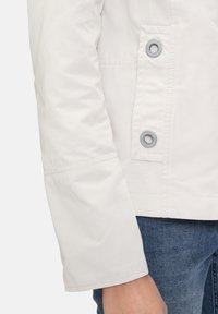 Lightweight white jacket with a smooth texture, featuring a button closure with gray accents and a side pocket.
