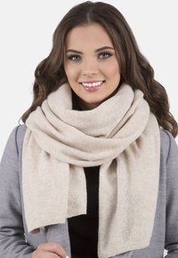Écharpe en laine beige avec une texture douce, enroulée lâchement autour du cou, avec un bord droit pour une finition soignée.