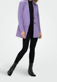 Lila muotoiltu bleiseri, jossa on kaksi etutaskua ja kaksi nappia; käytettävä mustan topin päällä ja yhdistetty mustiin housuihin ja nilkkureihin.