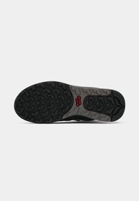Sole di scarpa da ginnastica nera con un motivo di grip testurizzato. Presenta un intersuola grigia e dettagli del logo rossi. La forma complessiva è arrotondata e flessibile.