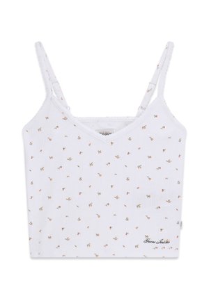 Camisole blanche courte avec fines bretelles ajustables, petit imprimé floral multicolore et logo "Guess Jeans" en bas à droite.