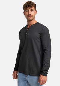 Langärmliges schwarzes Henley-Shirt aus weicher Baumwolle, mit einer Knopfleiste und einem lässigen Schnitt, kombiniert mit hellblauen Jeans.