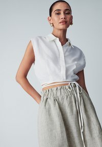 Valkoinen lyhythihainen, kauluksellinen crop-top, yhdistettynä vaaleanharmaisiin korkeavyötäröisiin pellavahousuihin, joissa on nyöriyksityiskohtia.