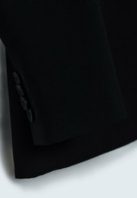 Černá upravená sako se rukávy z hladké látky, se strukturovaným tvarem a čtyřmi černými knoflíky jako detail zapínání.