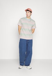 Camiseta a rayas en colores pastel, combinada con unos jeans de mezclilla holgados. Acabada con una gorra rosa y un collar de cadena plateada, calzado informal completa el look.