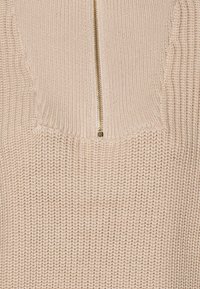 Beige gebreide trui met een halve ritssluiting, geribde halslijn en een gestructureerd stofpatroon, met een duidelijke, gestructureerde vorm.